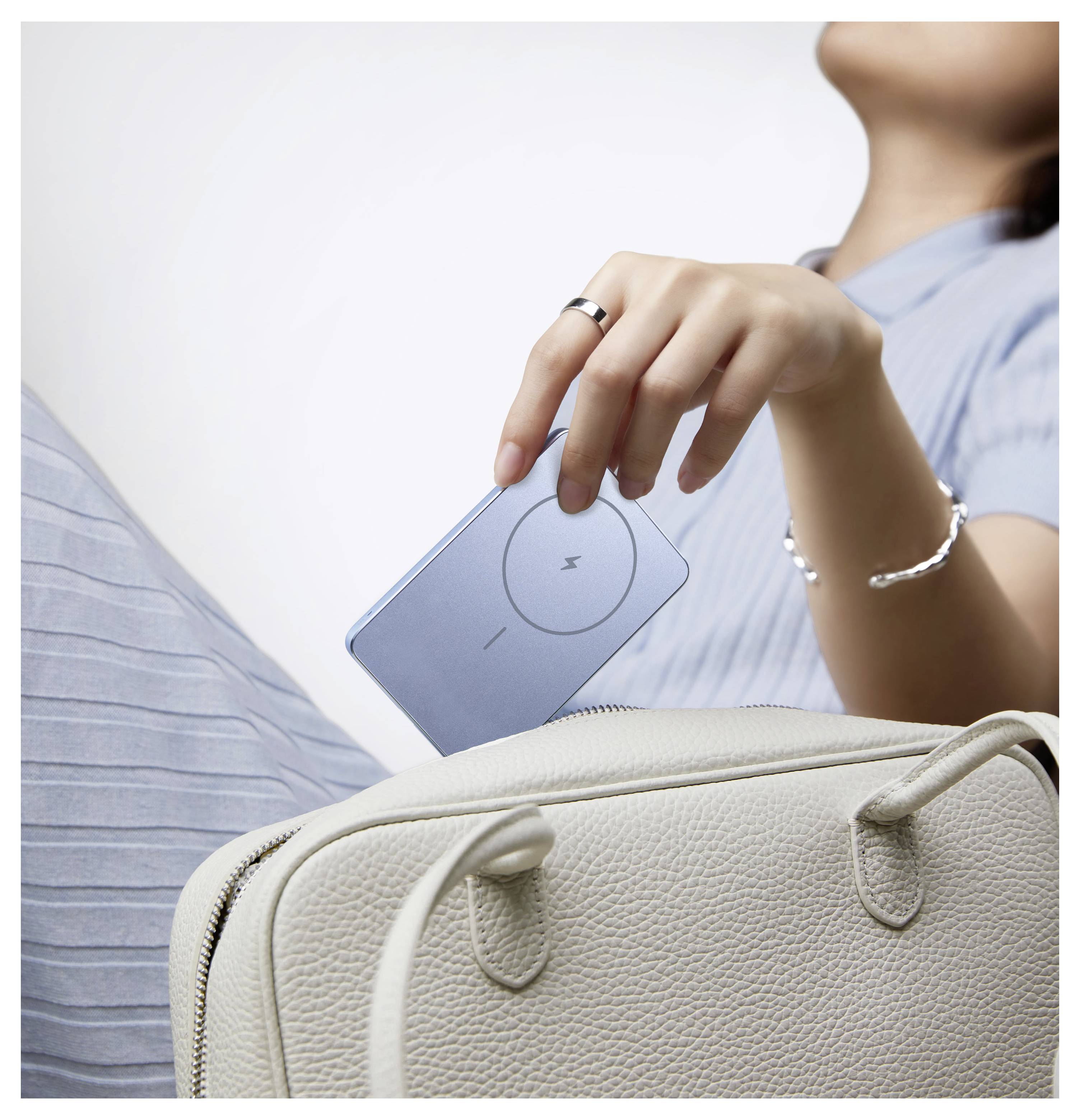 Eine Frau in einem blauen Hemd hält eine blaue Karte über einer cremefarbenen Handtasche und deutet damit an, dass sie packt oder sich zum Aufbruch vorbereitet.