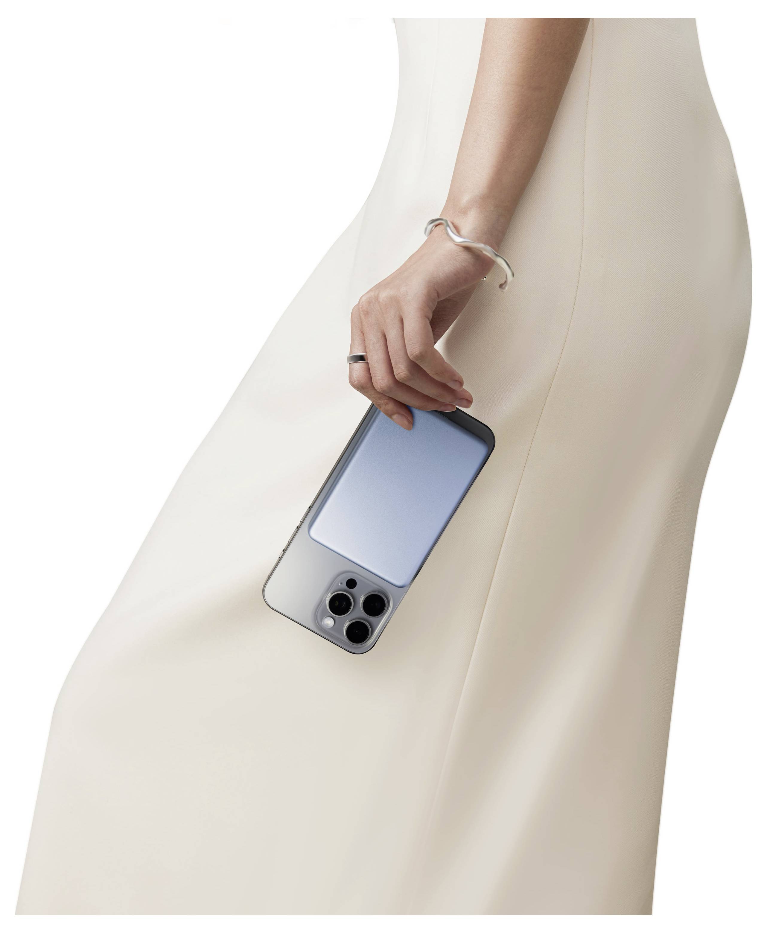 Nahaufnahme einer Frau in einem beigefarbenen Kleid, die ein Smartphone an ihrer Seite hält, wobei die Rückseite des Telefons und ihr Armband zu sehen sind.