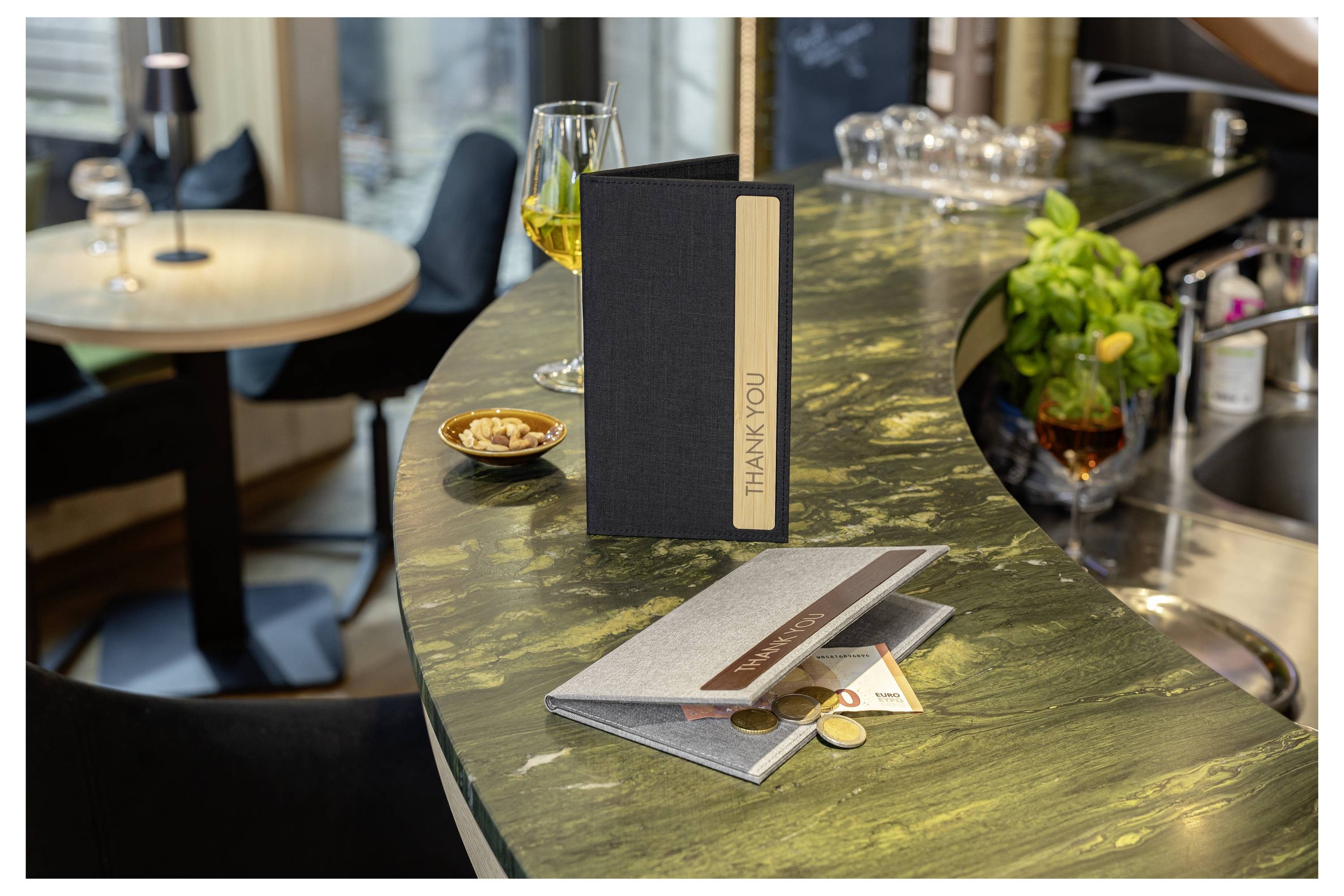 A restaurant counter with a standing 'THANK YOU' sign, folded menus, a wine glass, and a small dish, suggesting a dining or checkout area.