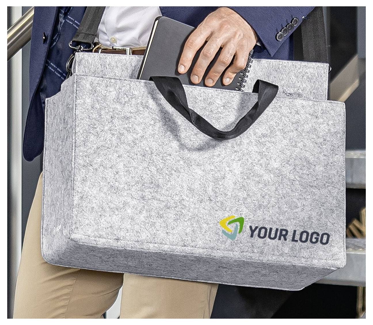 Person, der eine graue Filz-Laptoptasche mit schwarzen Griffen und einem Platzhalter „IHR LOGO