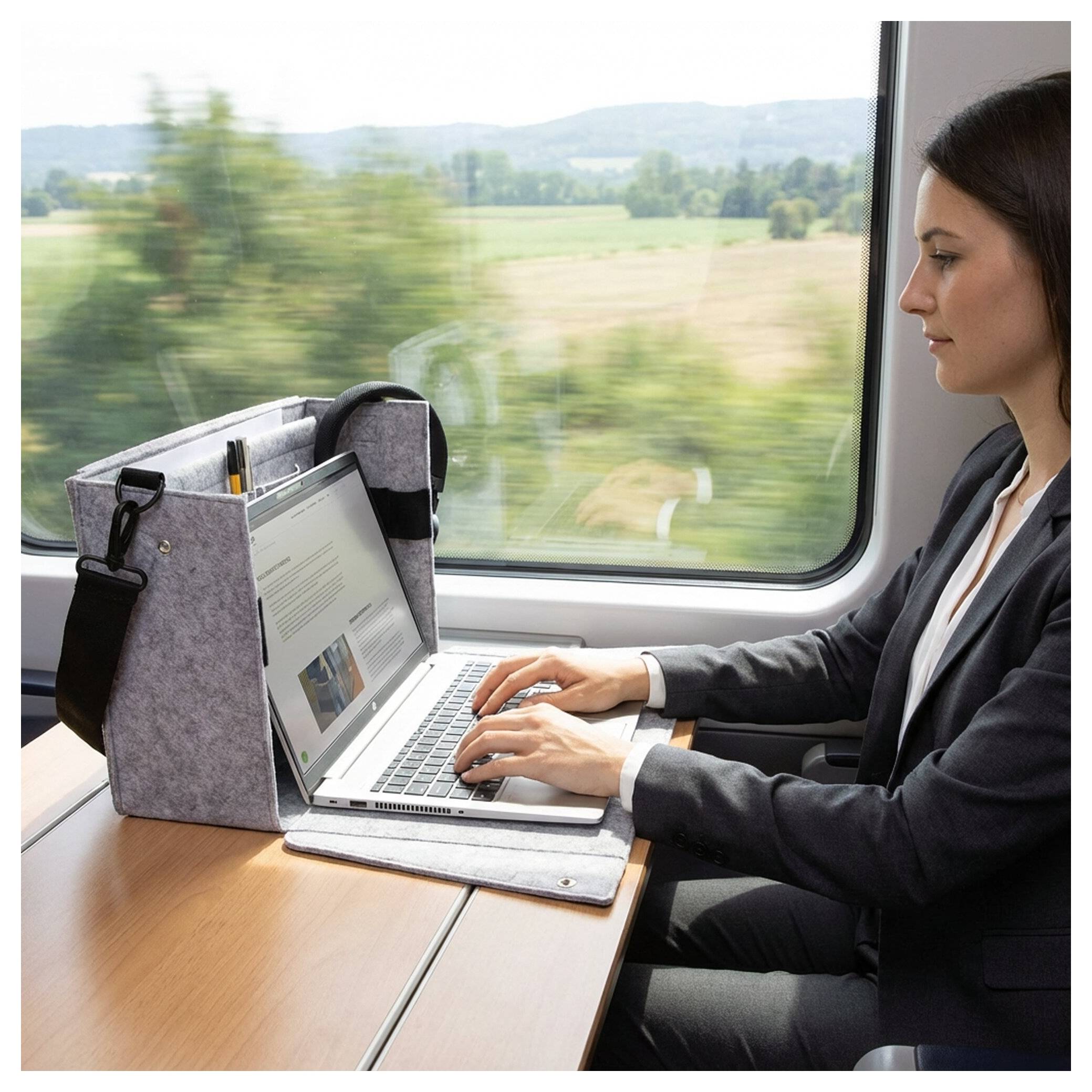 Frau arbeitet an einem Laptop auf einem Zugsitz neben einem Fenster, mit unscharfer Landschaft außerhalb.