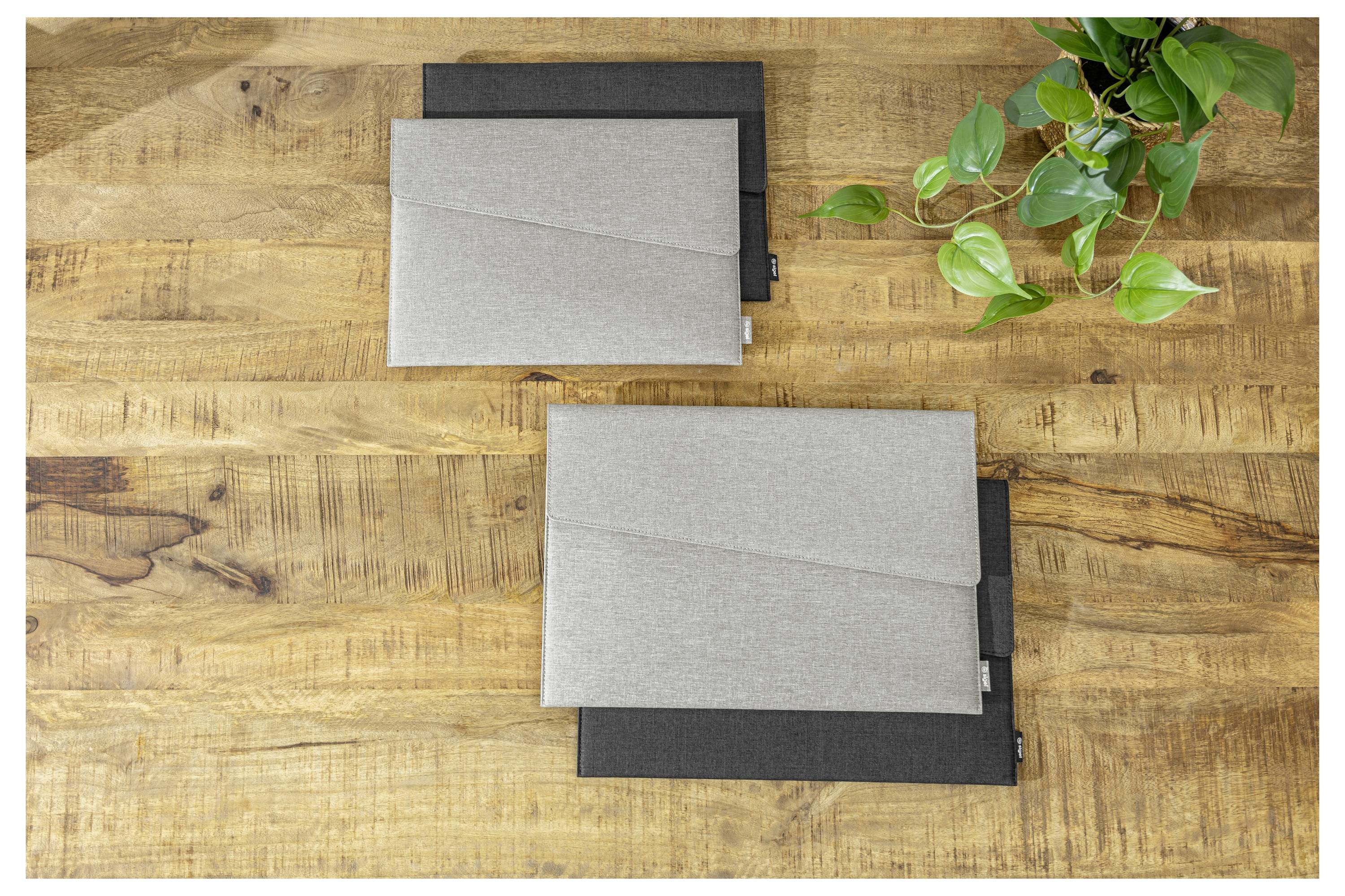 Zwei geschlossene graue Präsentationsmappen übereinander gestapelt auf einem Holztisch neben einer grünen Pflanze.