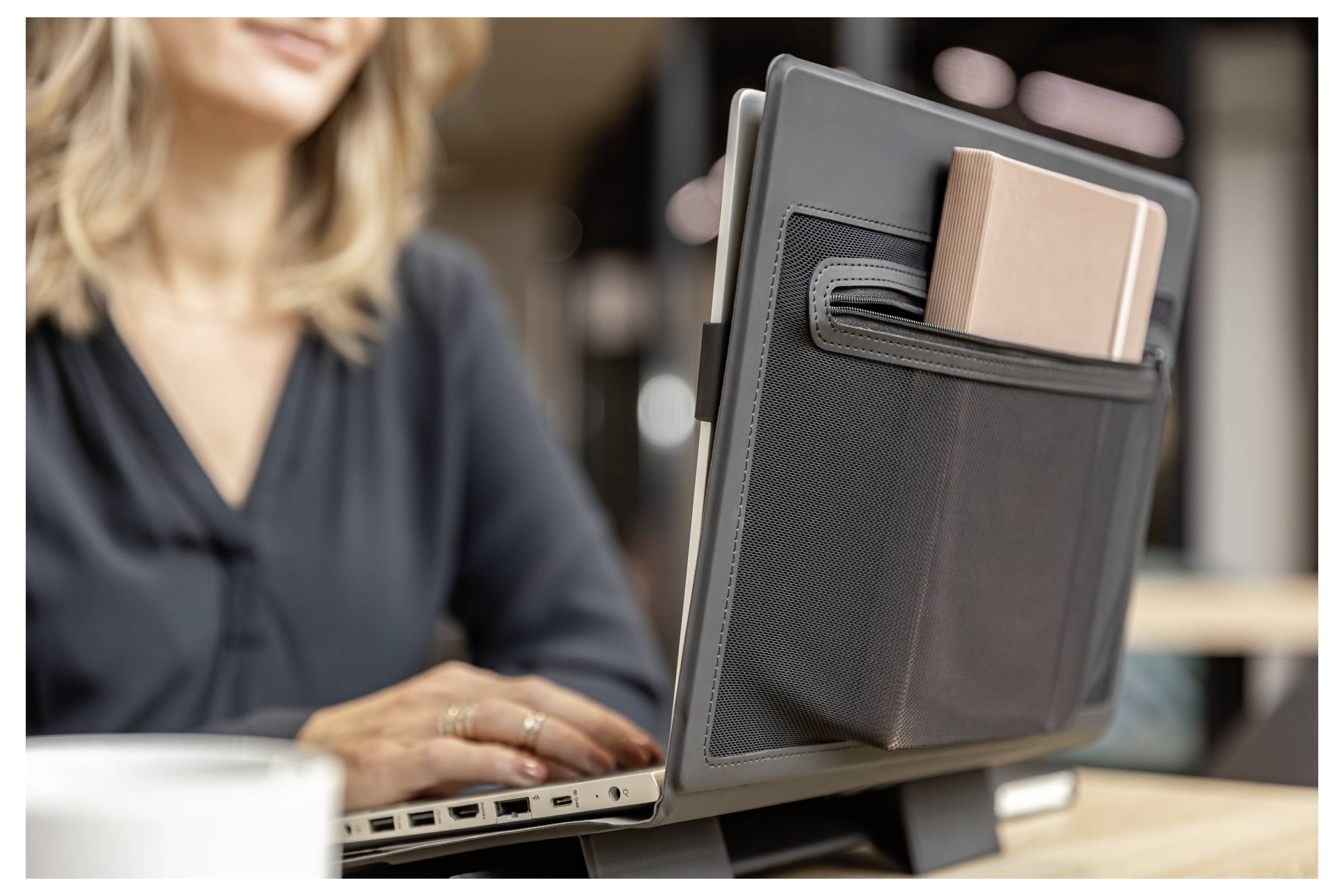 Person, die an einem Laptop arbeitet, mit einem Tablet, das hinter dem Bildschirm befestigt ist, was einen tragbaren Multi-Geräte-Arbeitsplatz in einem Büro oder Café andeutet.