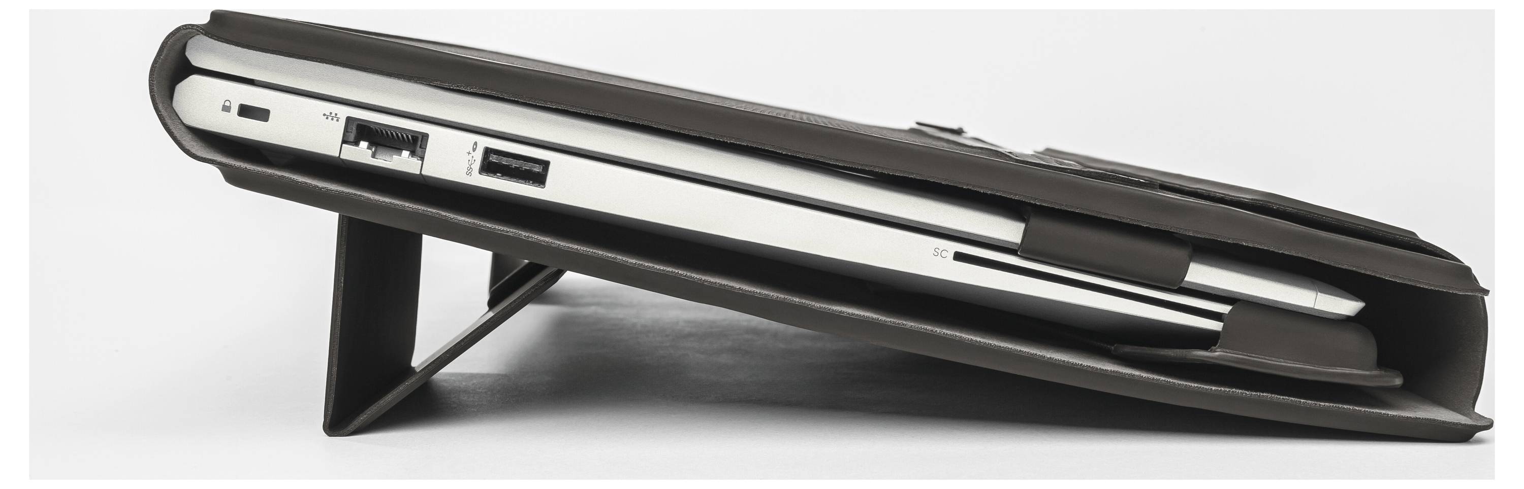 Geschlossener Laptop, seitlich dargestellt, ruht auf einem Ständer oder Keil mit sichtbaren Anschlüssen entlang der Kante.