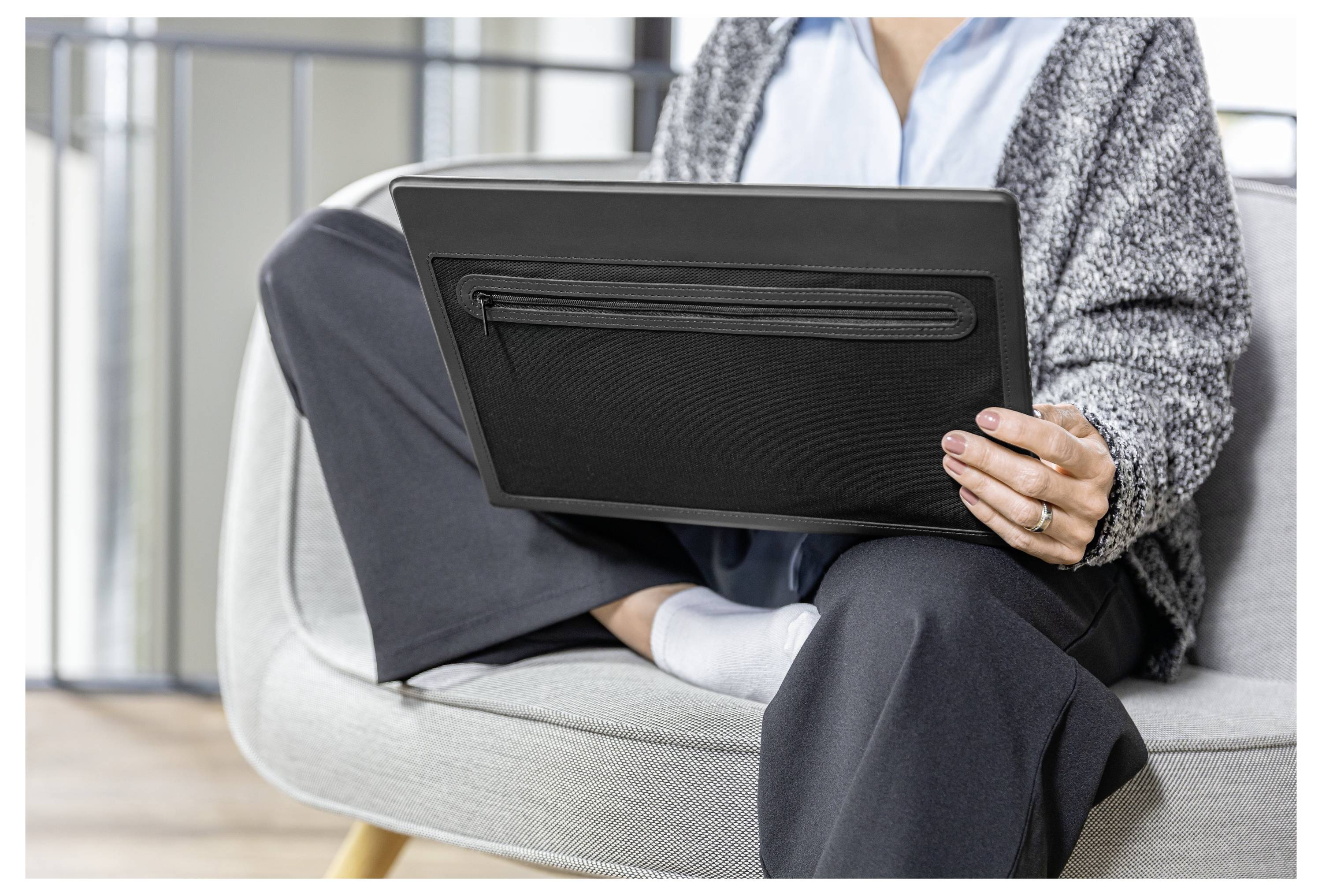 Person sitzt auf einem Stuhl und benutzt einen Laptop, mit überkreuzten Beinen in einer ungezwungenen Innenraumkulisse.