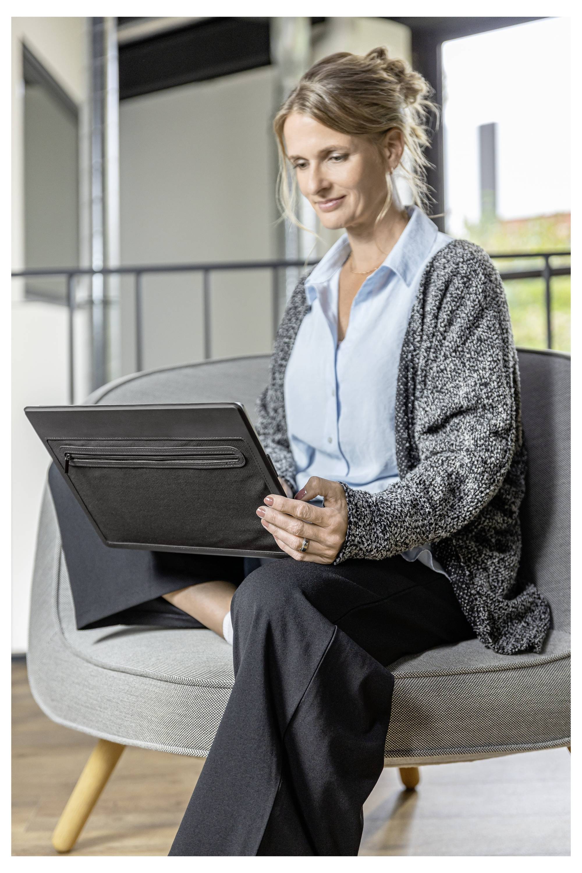 Eine Frau sitzt auf einem Stuhl und benutzt ein Tablet in einem modernen Büro- oder Loungebereich.