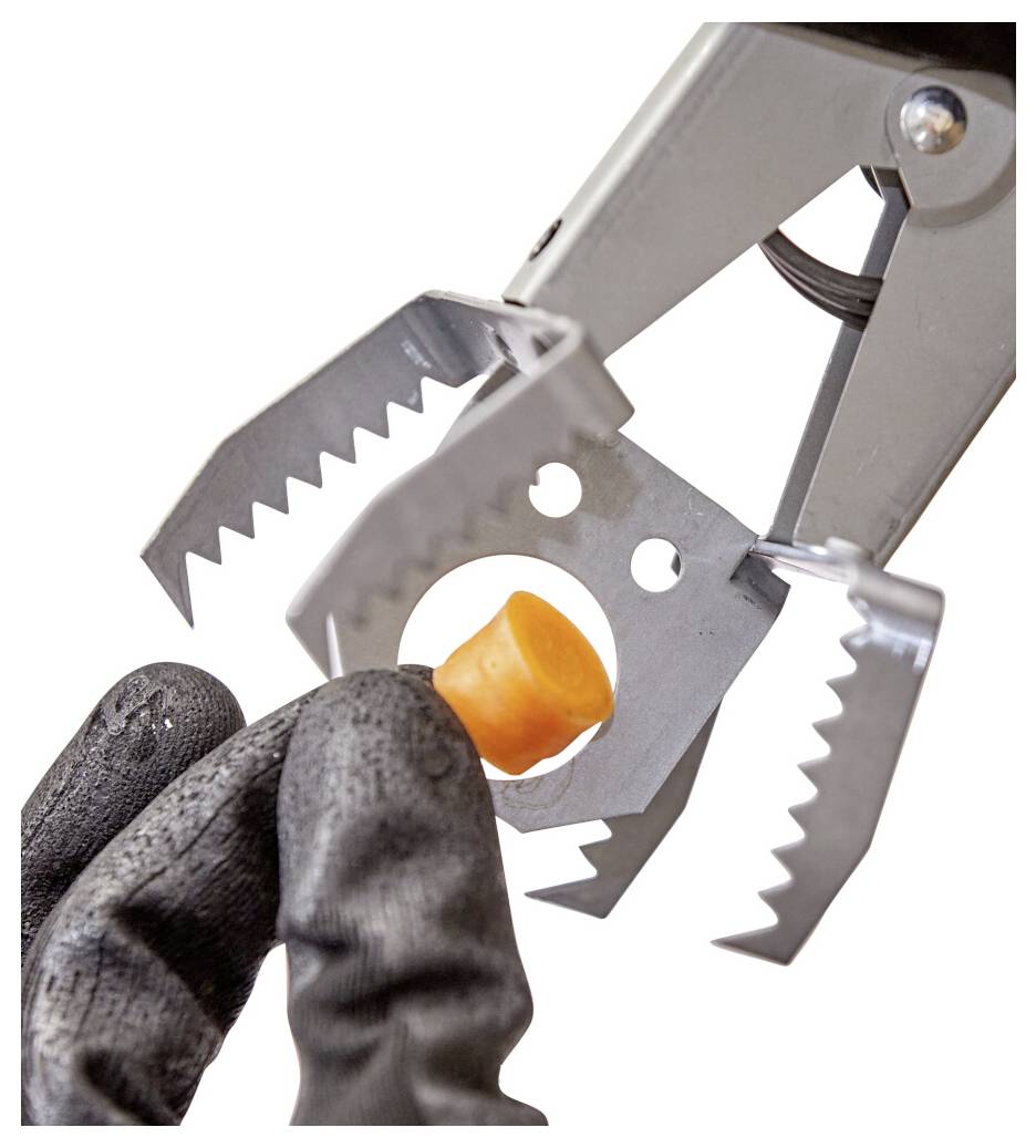 Behandschuhte Finger platzieren einen kleinen orangefarbenen Stopper in ein Metallgreifwerkzeug mit gezahnten Backen, Nahaufnahme auf weißem Hintergrund.