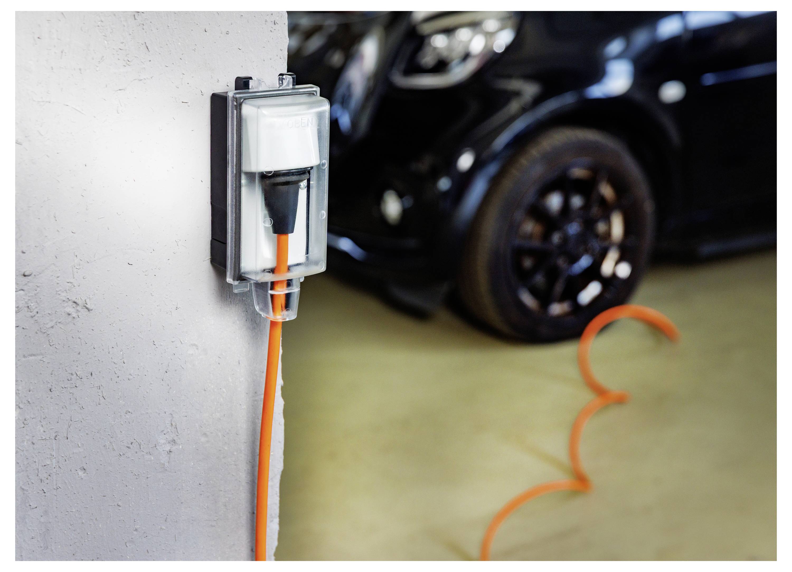 Elektrofahrzeug-Ladestecker an einem wandmontierten Ladegerät angeschlossen, mit einem schwarzen Auto im Hintergrund geparkt.