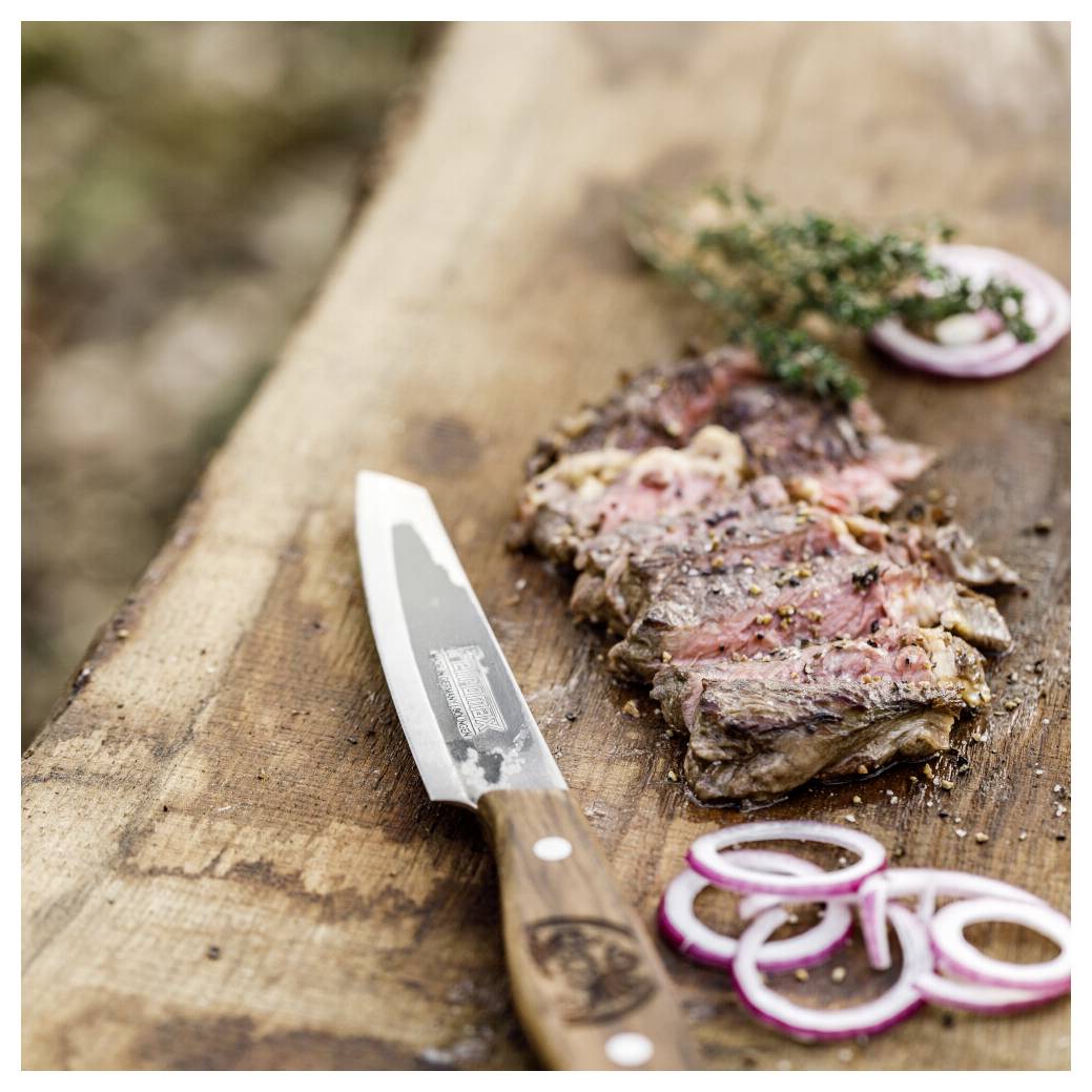 Geschnittenes gegrilltes Steak auf einem Holzschneidebrett mit einem Tranchiermesser, Rotzwiebel ringen und einer Kräutergarnitur.