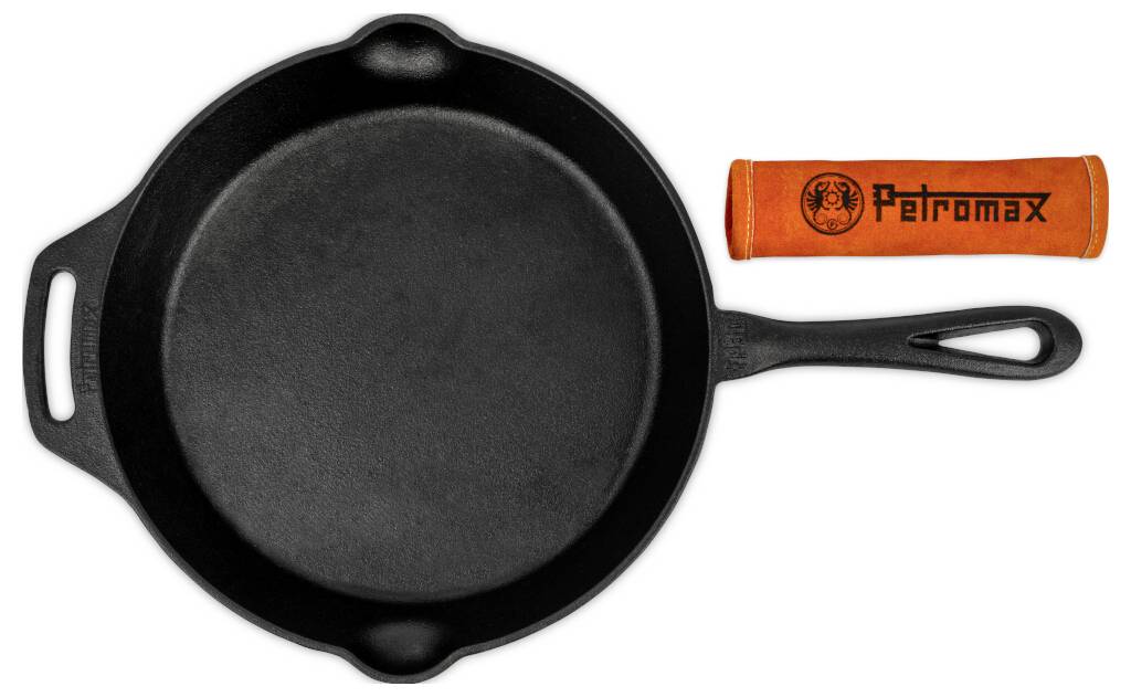 Schwarze Gusseisenpfanne mit zwei Griffen neben einer orangefarbenen 'Petromax'-Griffschutzkappe auf weißem Hintergrund.