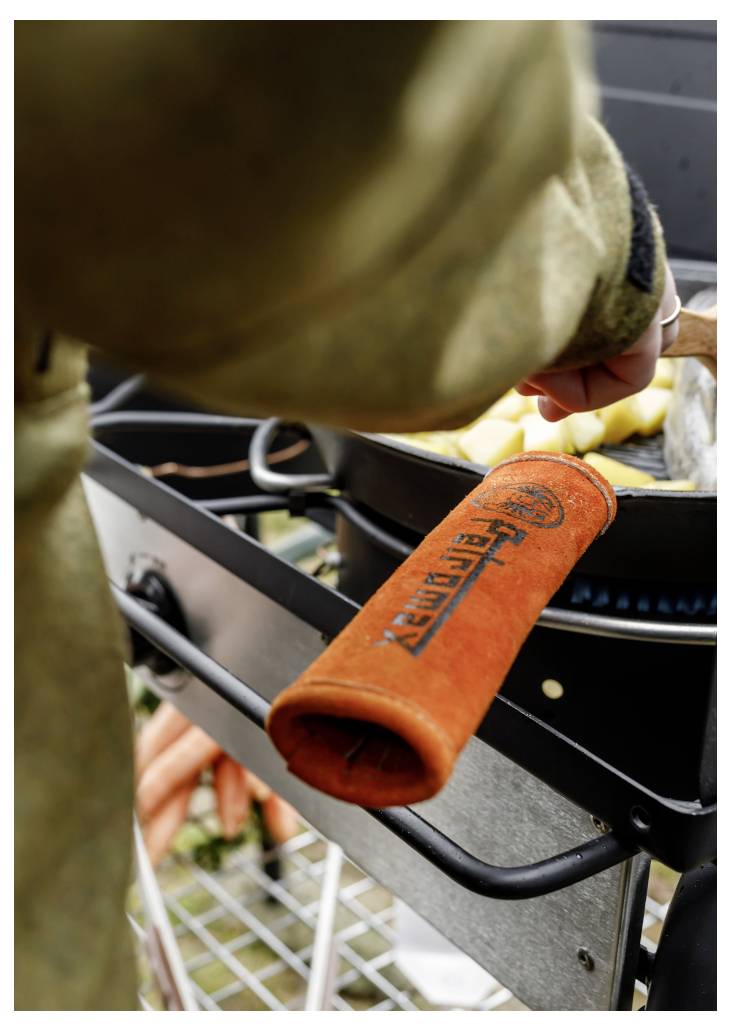 Person, die mit orangefarbigen Zangen Lebensmittel auf einem kleinen Außengrill oder Ofen zubereitet.