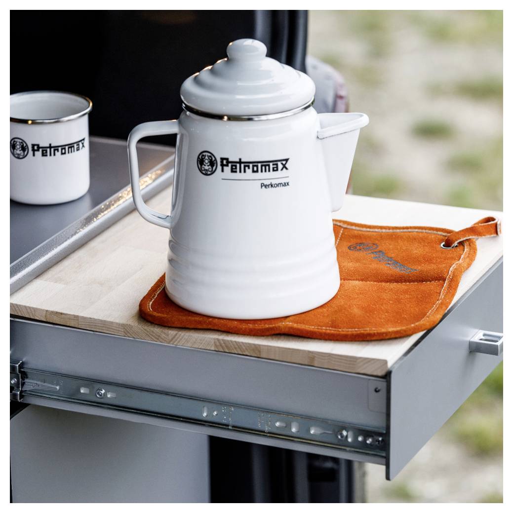 Weiße Emaille-Kaffeekanne auf einer orangefarbenen Matte auf einem ausziehbaren Campingküchenregal, mit passendem Becher daneben.