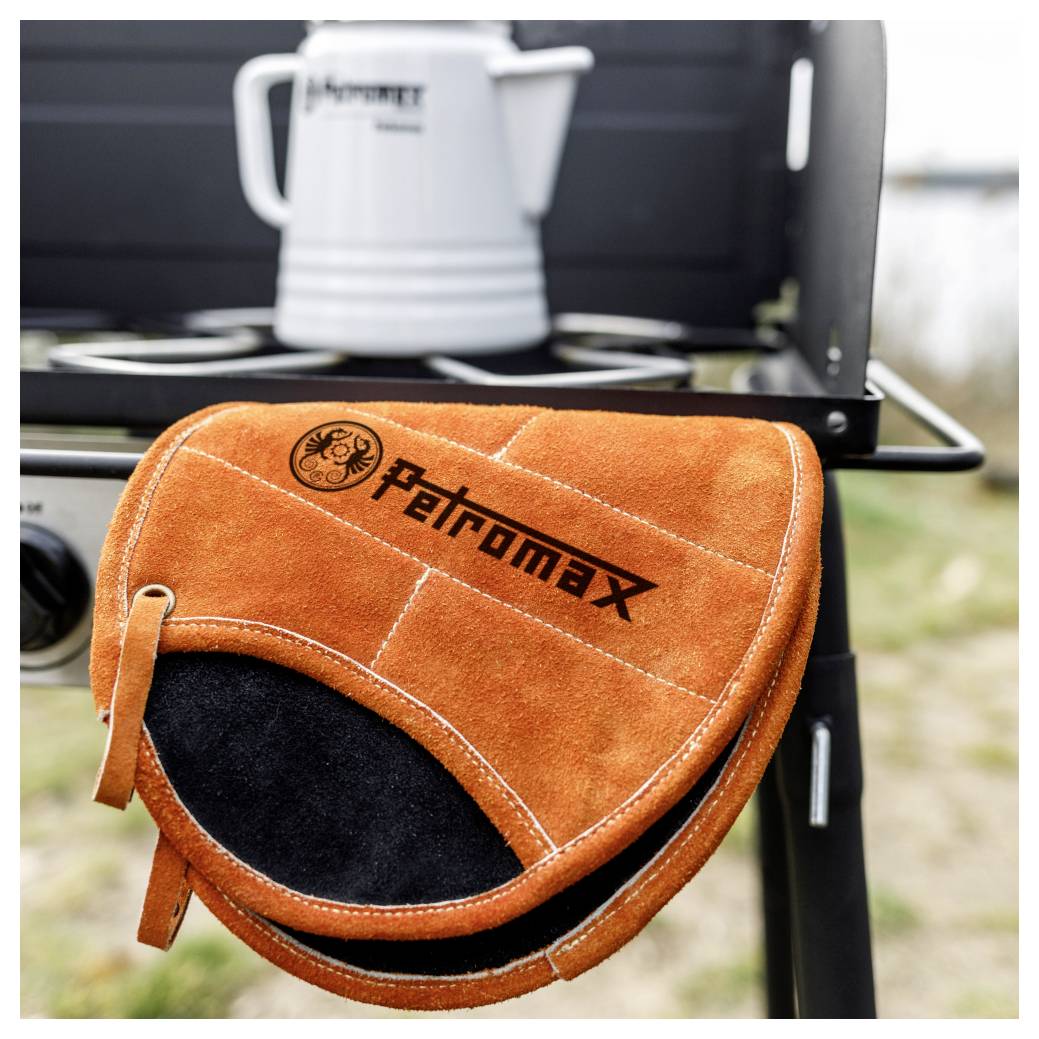 Orangener 'Patromax' Lederhandschuh, der an einem tragbaren Grill hängt, mit einem weißen Kessel-förmigen Topf auf dem Rost dahinter.