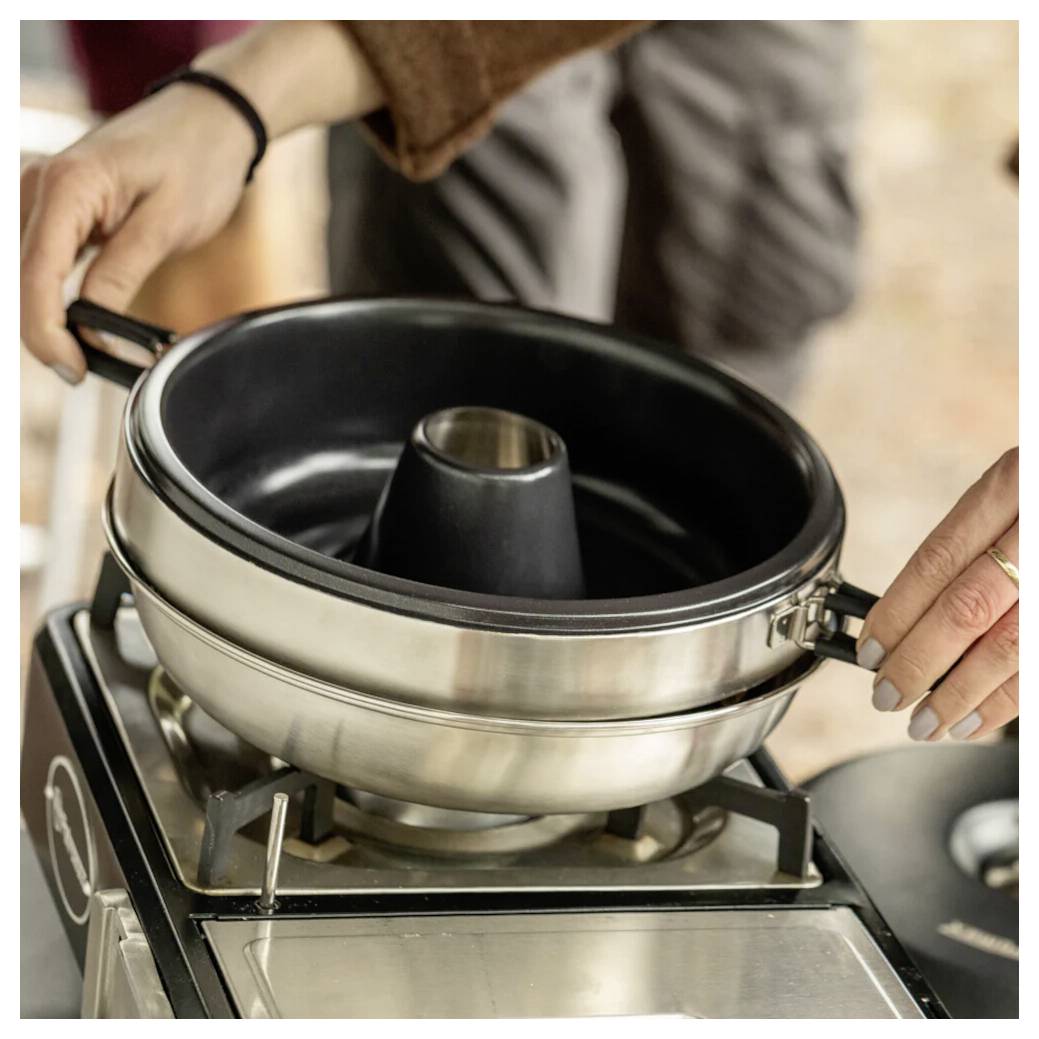 Hände, die eine Metallkugelhopfenform auf einem Kochfeldregler einstellen, sie zum Backen oder Kochen positionieren.