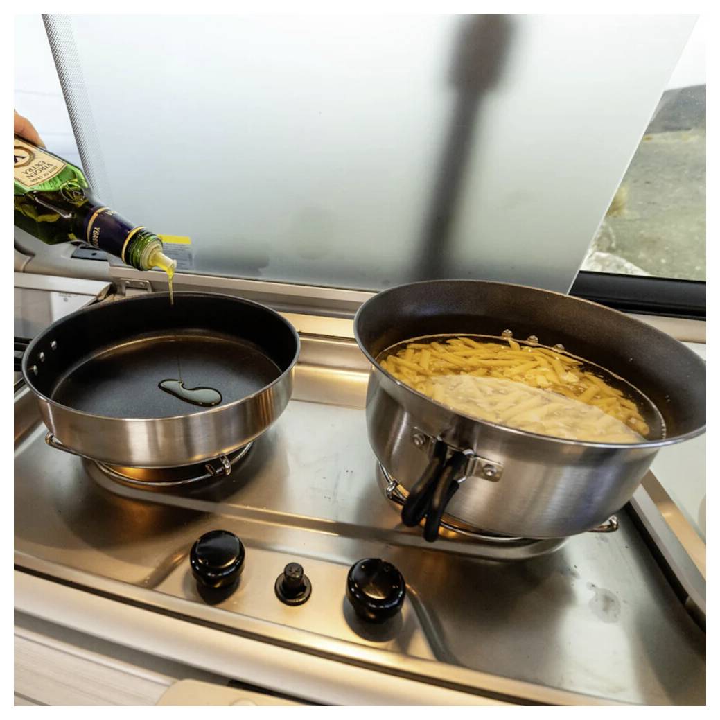 Kochen auf der Kochplatte: Öl wird in eine Bratpfanne neben einen Topf mit kochenden Pommes frites gegossen.