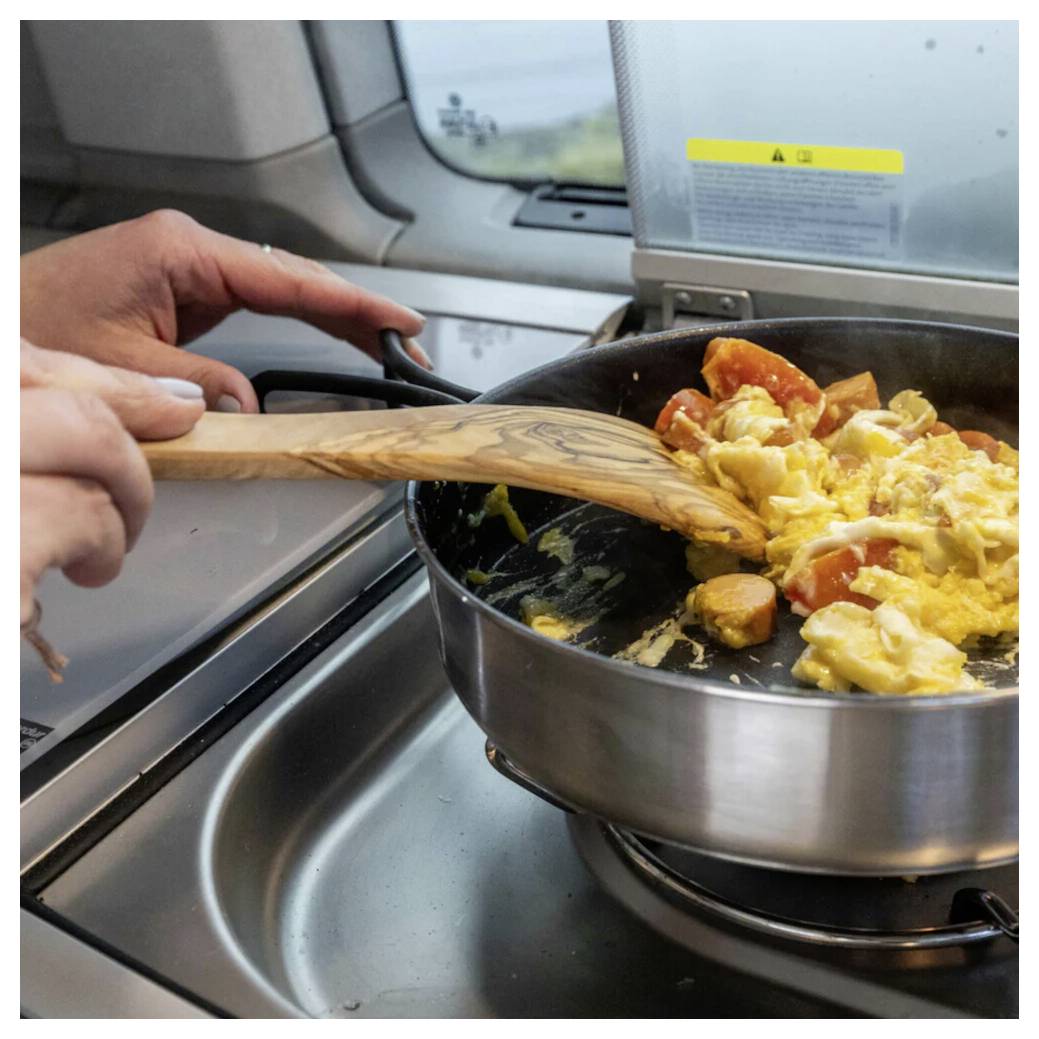 Mit der Hand Rührei und in Scheiben geschnittene Wurst in einer Pfanne auf einem Kochfeld in einem Zugküchenbereich umrühren.