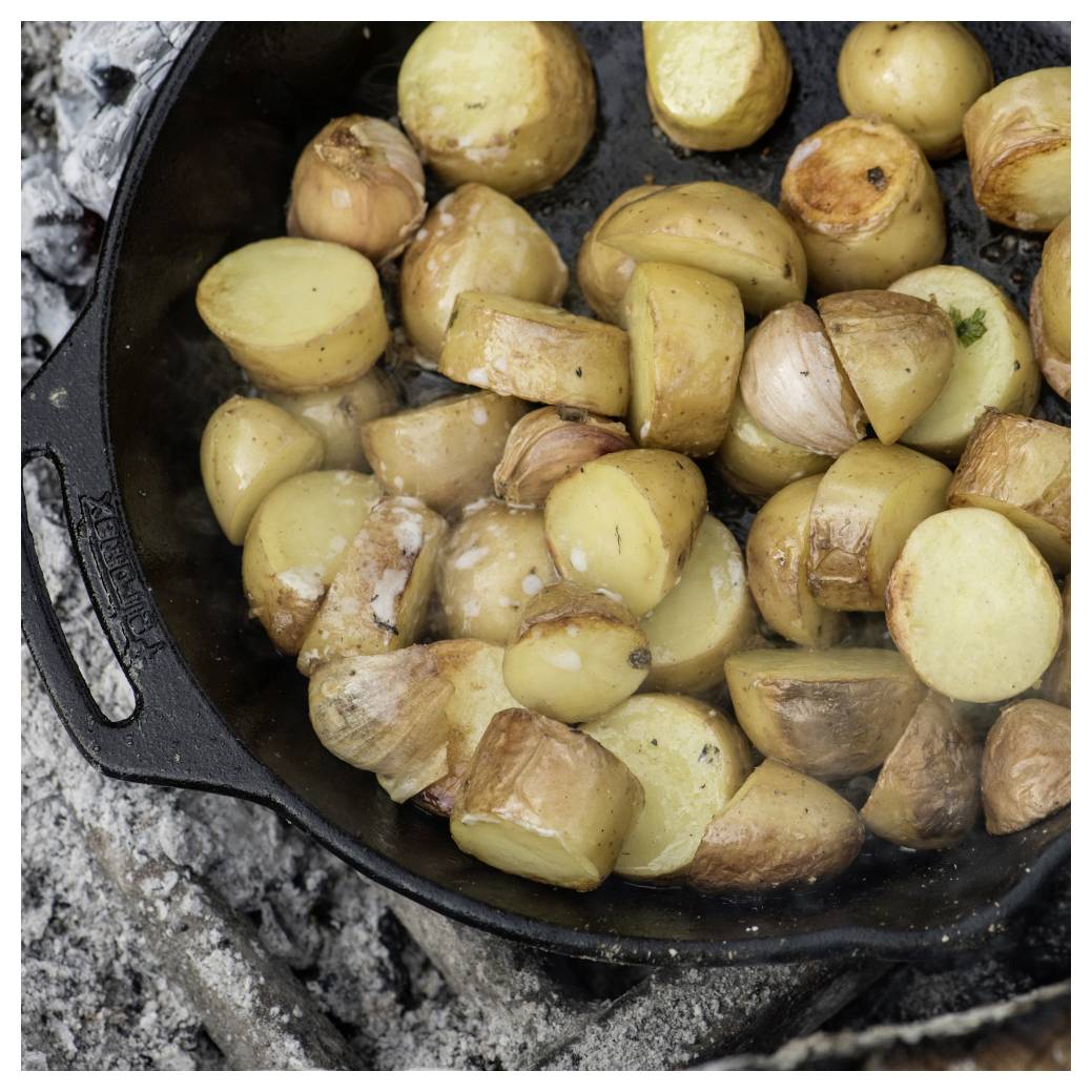 Geröstete Kartoffelhälften und Knoblauchzehen, die in einer gusseisernen Pfanne zischen.