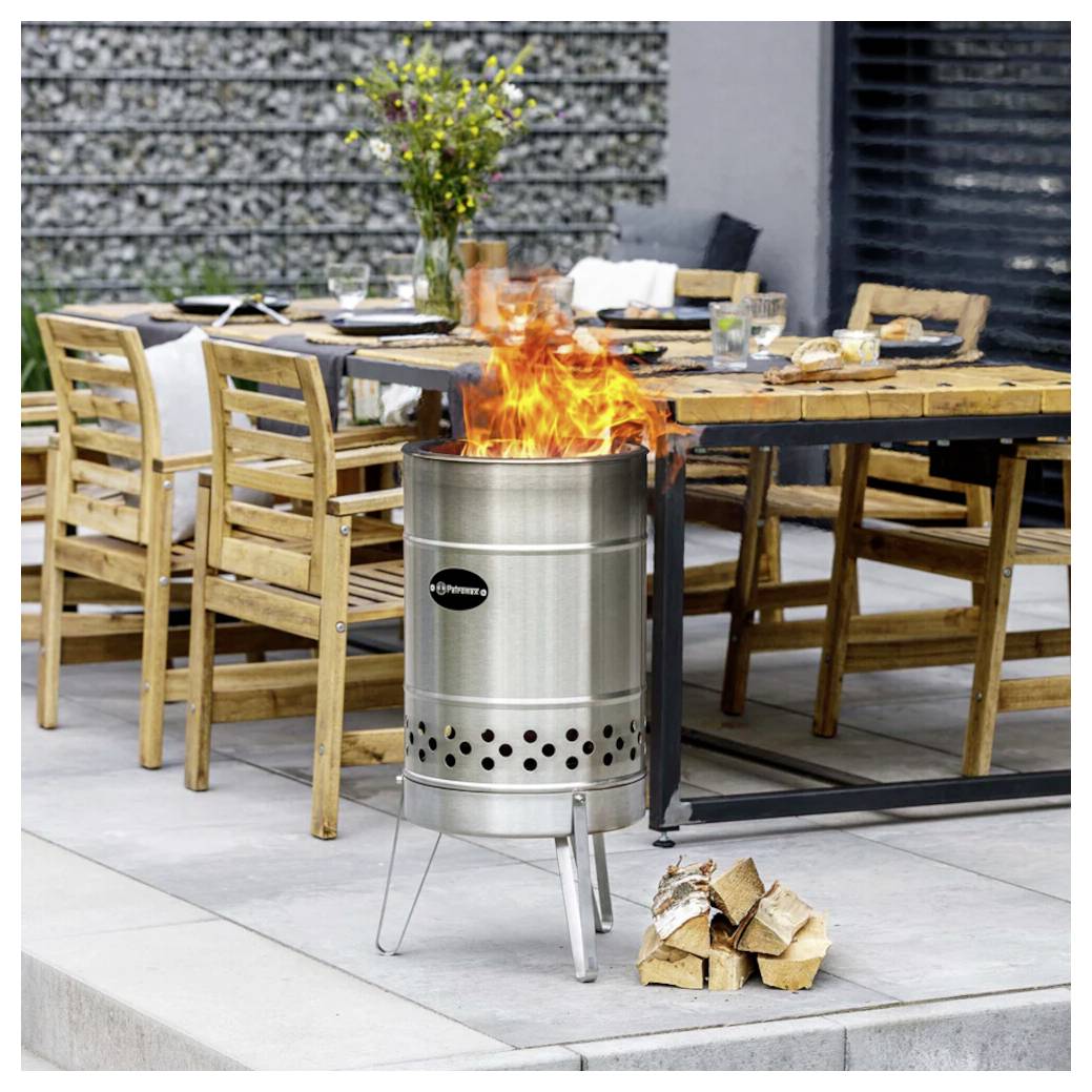Tragbares Metall-Feuerrost, das neben einem Außenesstisch brennt, mit gestapeltem Brennholz auf einer Terrasse.