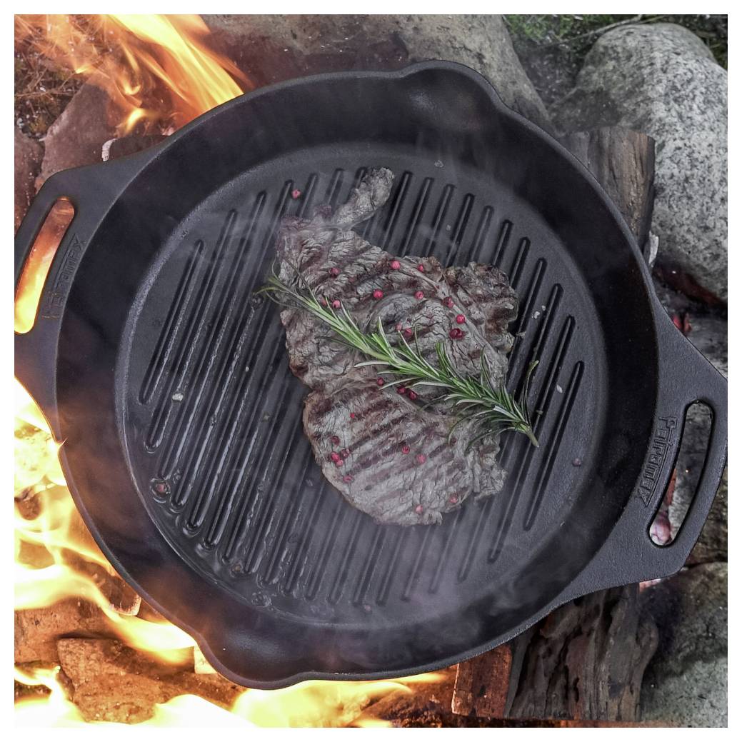 Steaks, die in einer gusseisernen Grillpfanne über offenem Feuer gebraten werden, belegt mit Rosmarin und Pfefferkörnern.