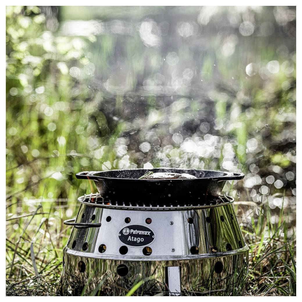 Tragbarer Campingkocher mit einer Pfanne obendrauf, aufgestellt in grüner Outdoor-Umgebung.