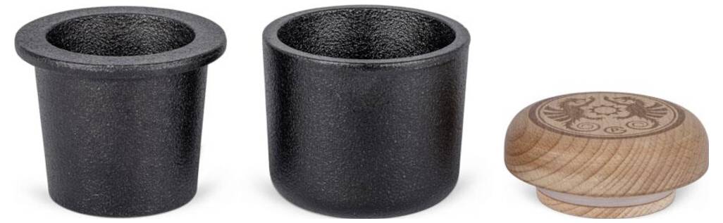 Zwei schwarze isolierte Tassen und ein kleiner runder Holzuntersetzer oder -deckel mit eingraviertem Blumenmuster.