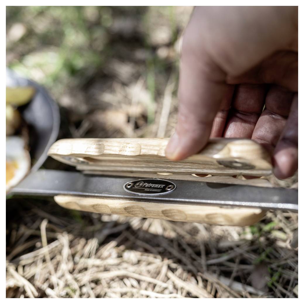 Hand hält ein Taschenmesser mit Holzgriff oder Multitool im Freien, mit teilweise geöffneter Klinge über trockenem Gras.