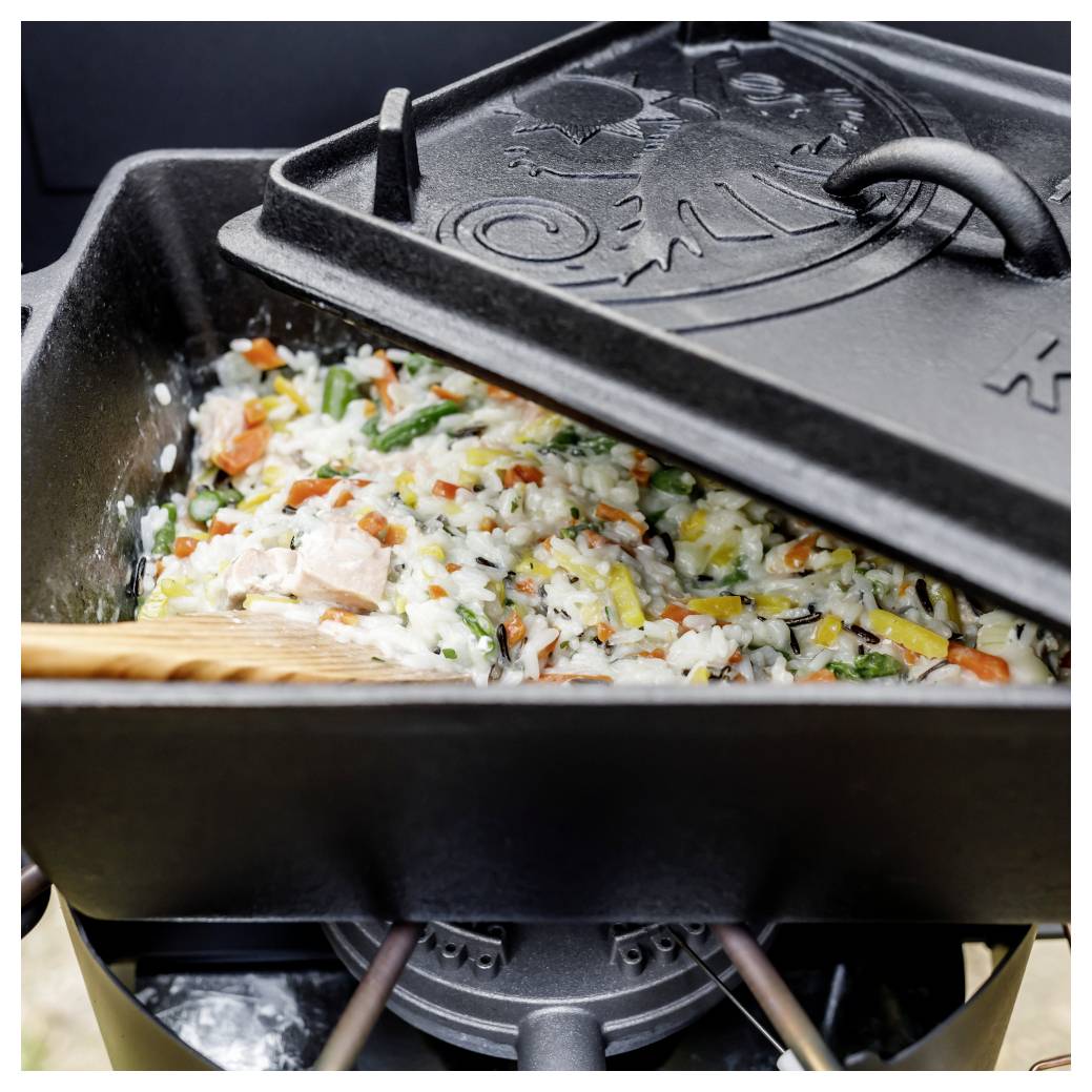 Reis, Gemüse und Hähnchen kochen in einem gusseisernen Topf mit teilweise geschlossenem Deckel auf einem Herd oder Grill.