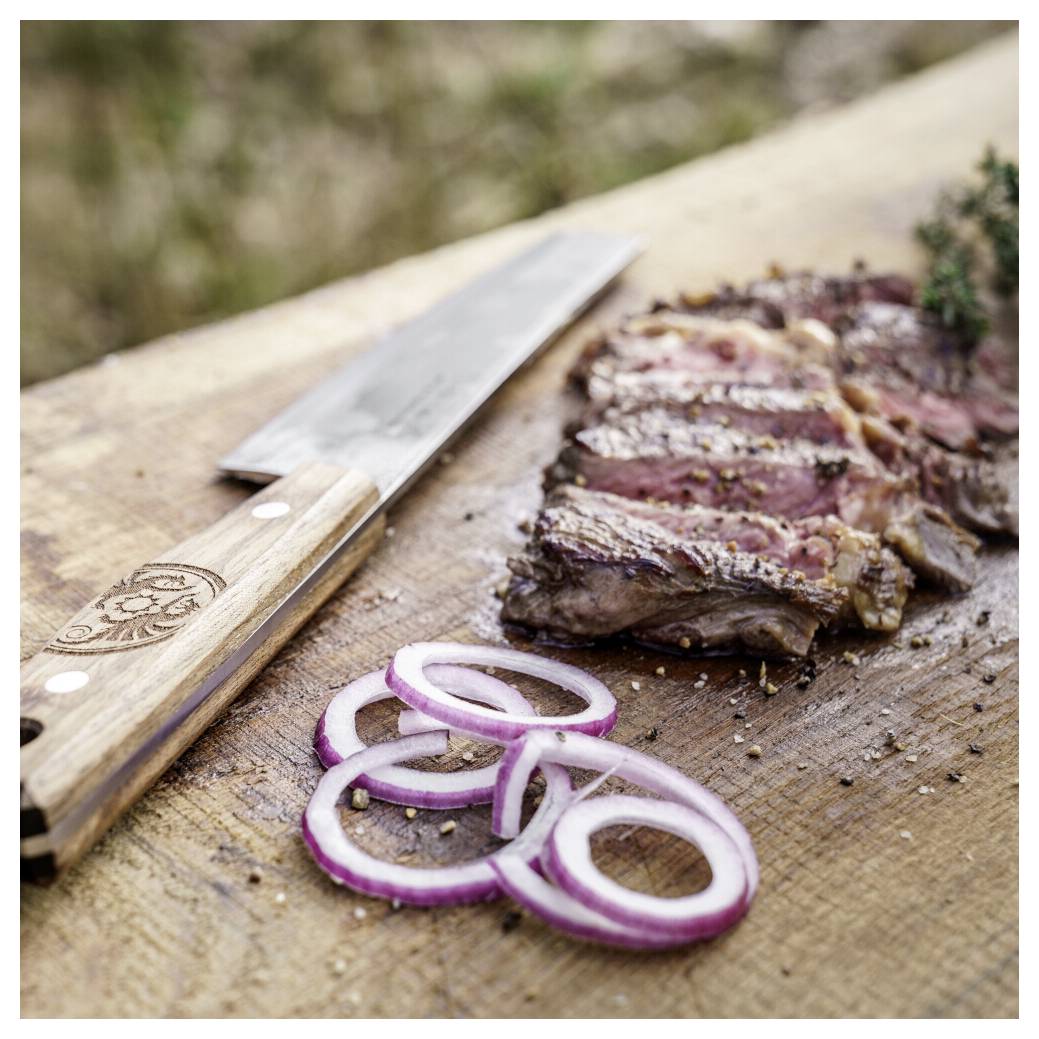 Geschnittenes gegrilltes Steak auf einem Schneidebrett mit einem Chefmesser und Rotzwiebel-Ringen im Vordergrund.