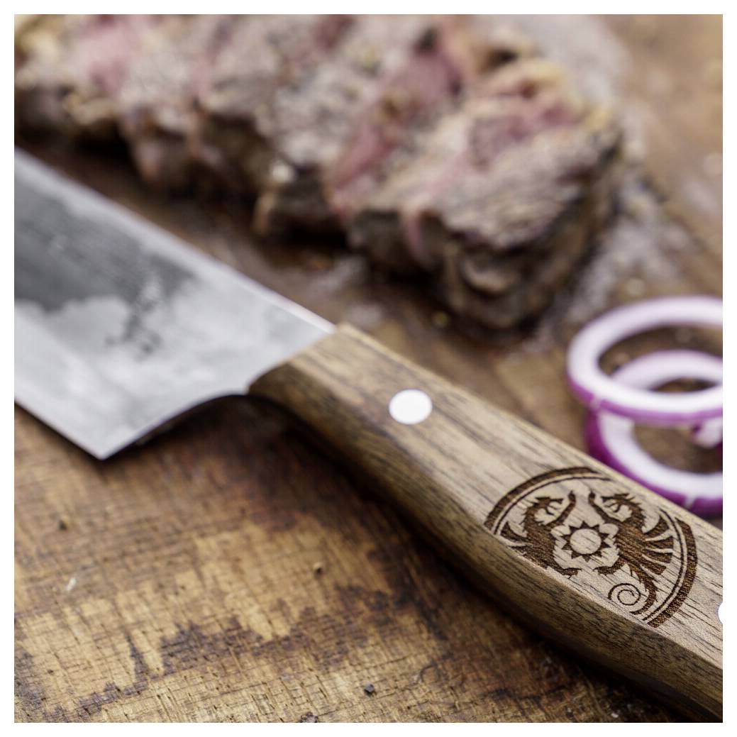 Nahaufnahme eines Küchenmessers mit hölzernem Griff auf einem Schneidebrett, mit unscharfem geschnittenem Fleisch und Zwiebelringen im Hintergrund.