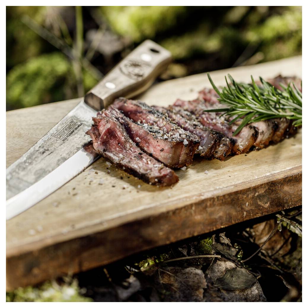 Geschnittenes gegrilltes Steak auf einem hölzernen Schneidebrett mit einem Messer und Rosmaringarnitur im Freien.