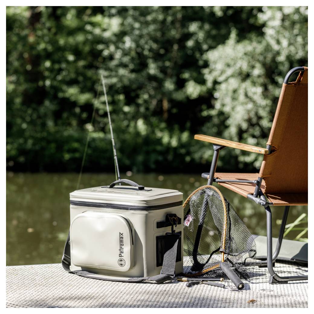 Angelausrüstung auf einem Steg am Wasser, mit einer Köderbox, einem Kescher, einer Angelrute und einem Stuhl.