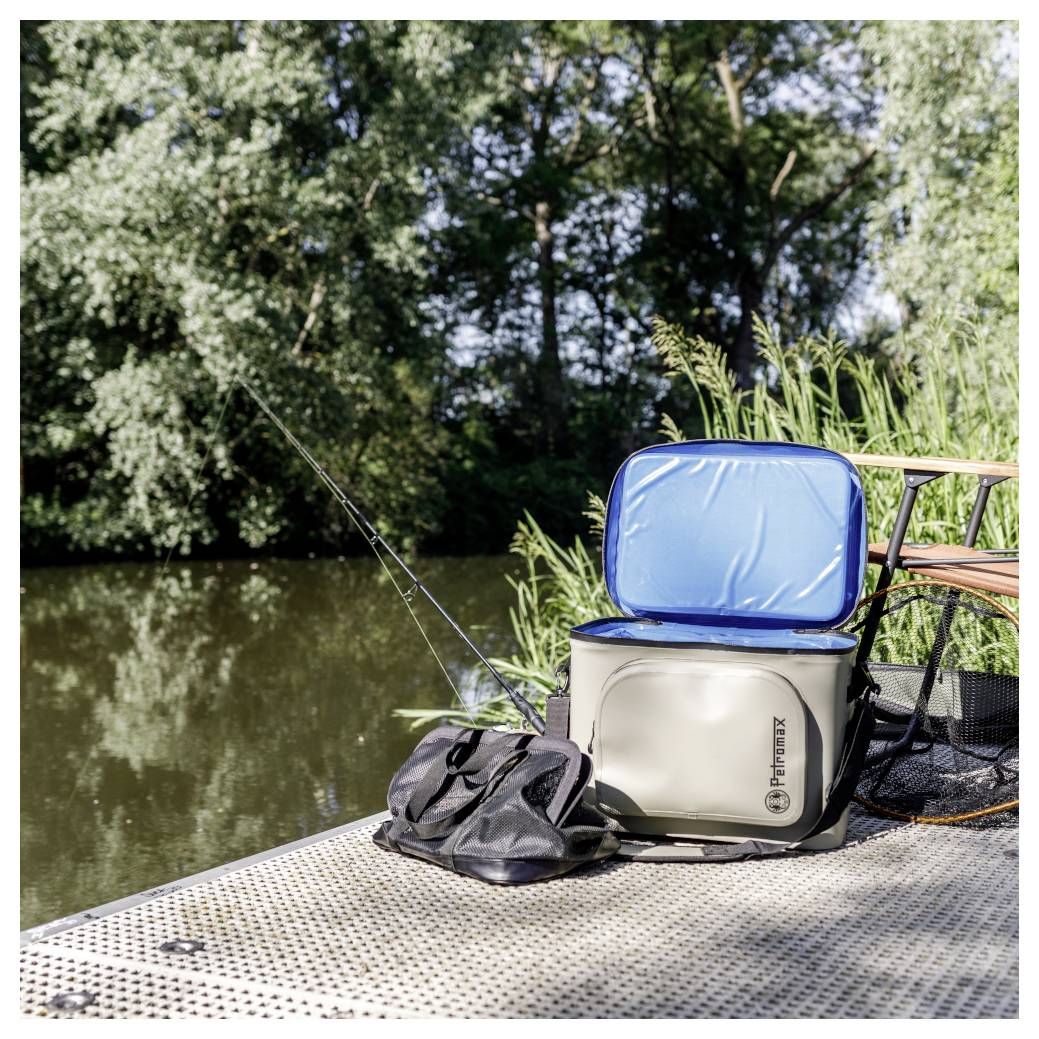Angelausrüstung auf einem Steg an einem Fluss, mit einer Kühlbox, einer Tasche und Angelruten neben dem Wasser.