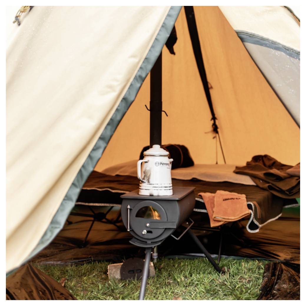 Campingkocher in einem Zelt, mit einem Wasserkessel oben drauf und einer Schlafausrüstung im Hintergrund.
