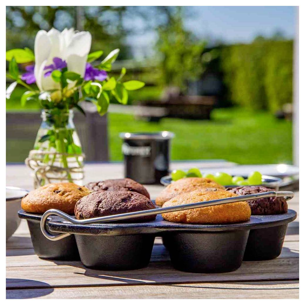 Frische Muffins in einem Backblech auf einem sonnenbeschienenen Tisch im Freien, mit einer Vase mit Blumen und einem unscharfen Garten im Hintergrund.