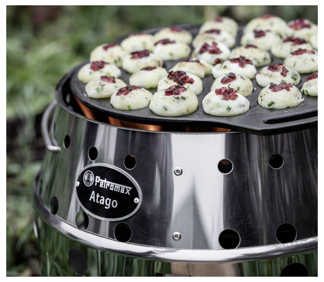 Outdoor-Grill mit runder Pfanne, auf der kleine Knödel oder gefüllte Häppchen mit Kräutern und roter Würzung auf einem Petromax Atago Kocher zubereitet werden.