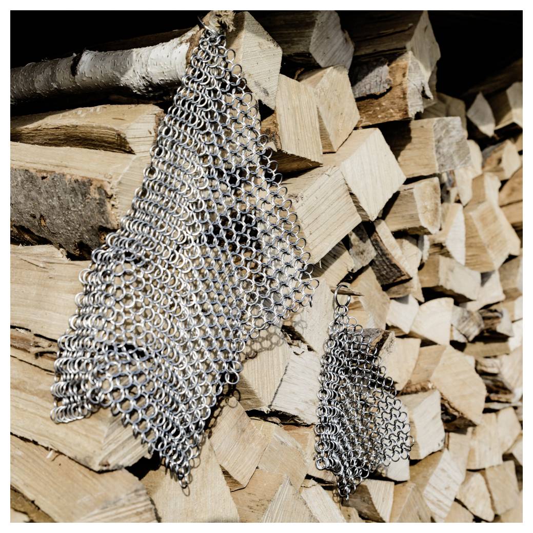 Zwei Metallkettenhemdstücke, die über einem gestapelten Haufen geschnittenem Brennholz hängen.