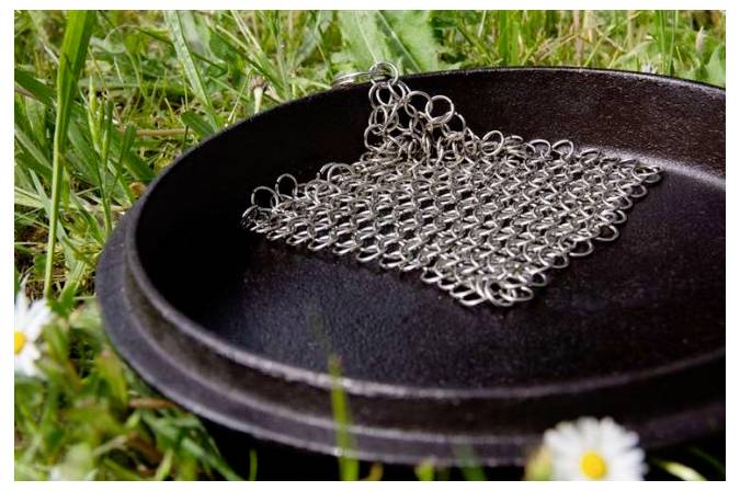 Metallisches Kettenpanzerstück ruht in einer schwarzen Pfanne im Freien auf Gras und deutet auf ein Reinigungs- oder Ausstellungsaufbau hin.