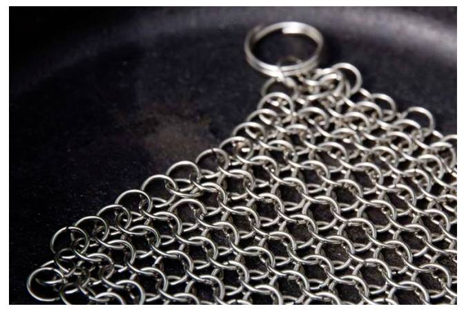 Nahaufnahme eines Metallkettenhemds oder Netzes aus untereinander verbundenen silbernen Ringen mit einem Schlüsselring oben auf dunklem Hintergrund.