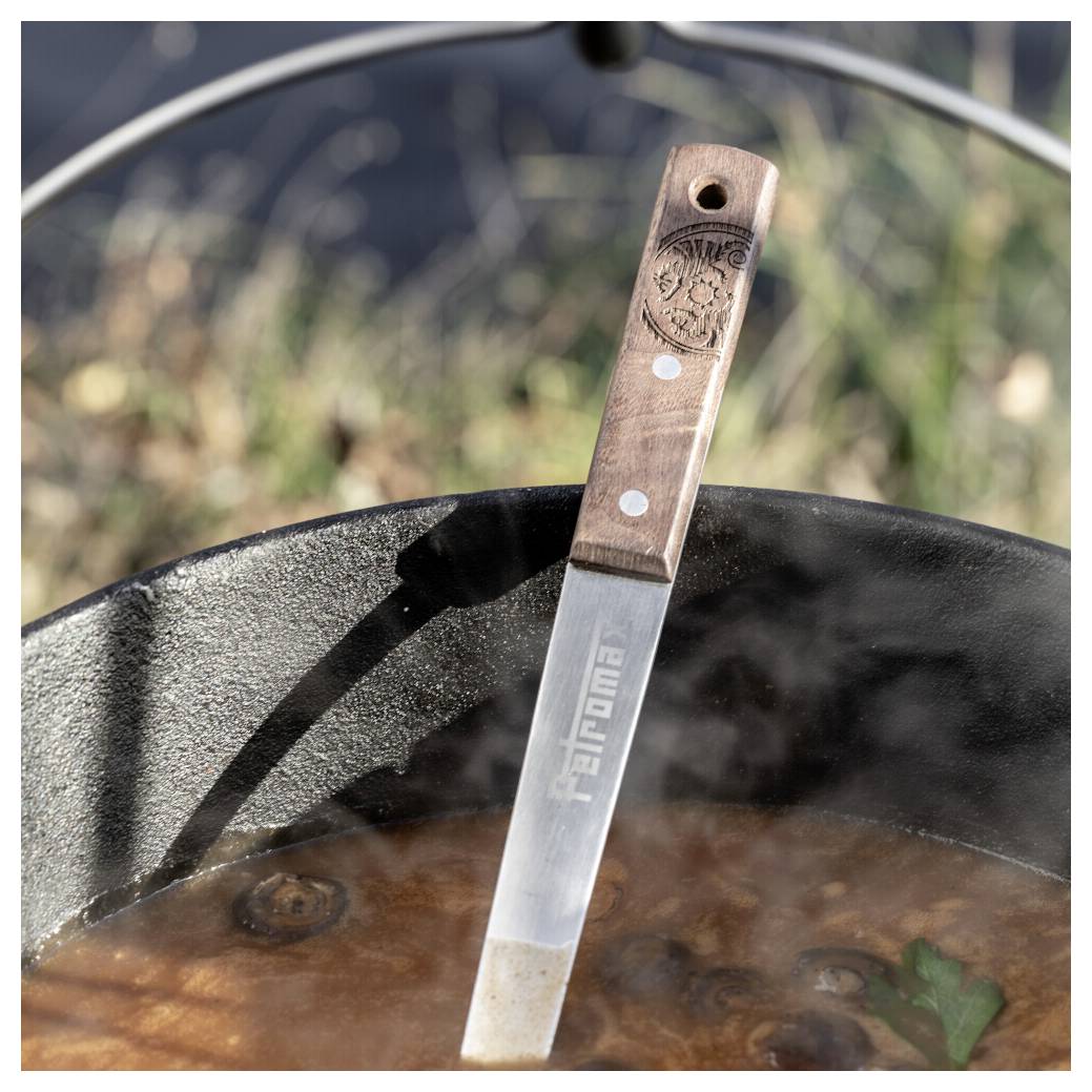 Messer mit Holzgriff ruht in einem dampfenden Topf mit köchelnder Suppe oder Eintopf im Freien.