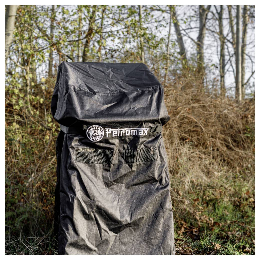 Schwarzer Petromax Outdoor-Grill oder -ofen mit einer schützenden Regenschutzhaube, stehend in einem grasbewachsenen Waldgebiet.