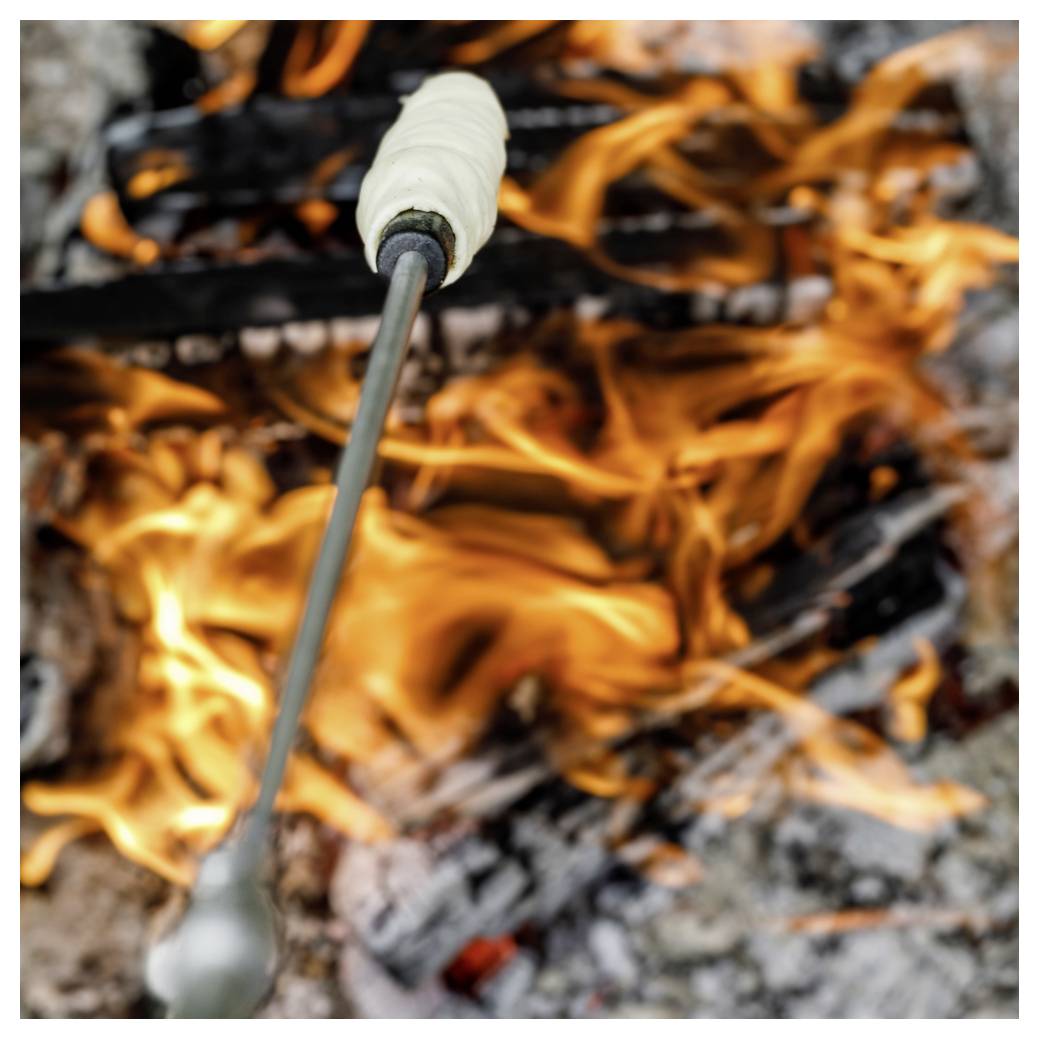 Marshmallows, die auf einem Stock über einem offenen Lagerfeuer geröstet werden, mit hellen Flammen und glühenden Kohlen.