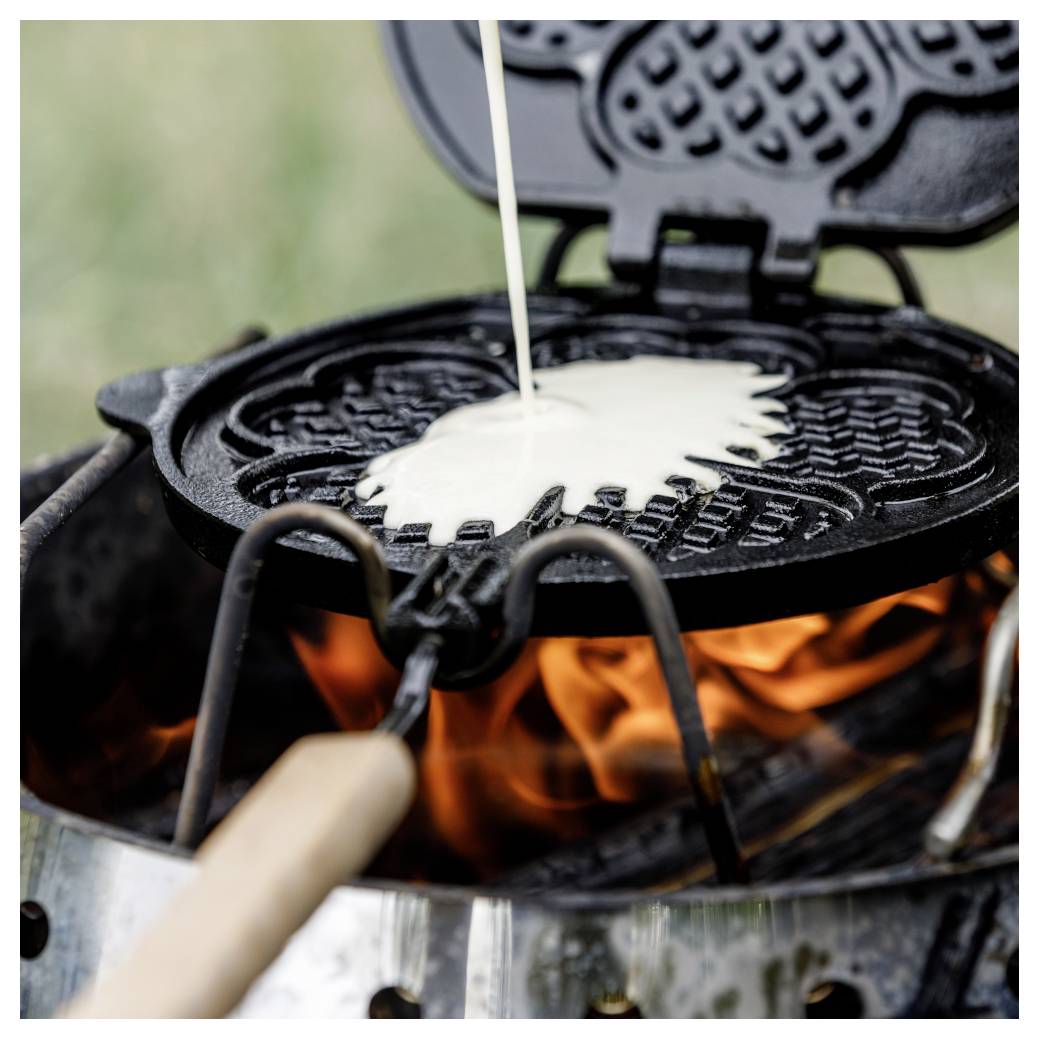 Waffelteig über offener Flamme in einem Waffeleisen backen, wobei der Teig in das heiße Eisen gegossen wird.