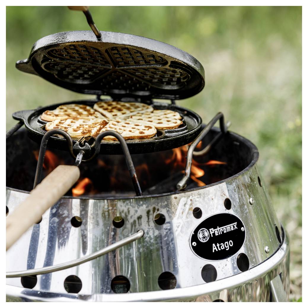 Ein Waffeleisen, das Waffeln über einer offenen Flamme auf einem tragbaren Outdoor-Grill zubereitet.