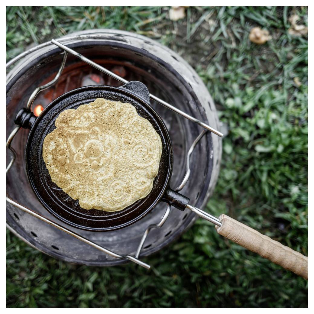 Tortilla oder Fladenbrot, das in einer Pfanne über einem Outdoor-Holzkohleherd gekocht wird, von oben betrachtet.