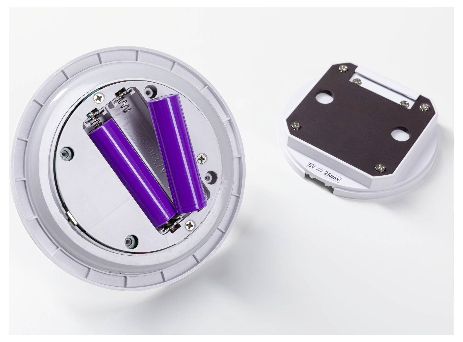Zwei lila zylindrische Batterien, die in einem runden weißen Gerätegehäuse montiert sind, daneben gezeigt mit einer separaten dunklen Abdeckplatte auf weißem Hintergrund.