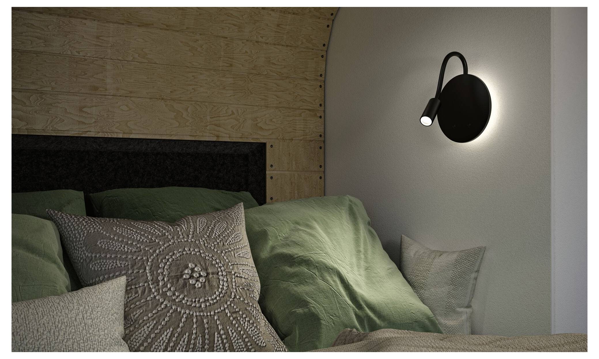 Ein Schlafzimmerbett mit grüner Bettwäsche und gemusterten Kissen, beleuchtet durch eine schwarze an der Wand montierte Leselampe auf der rechten Seite.