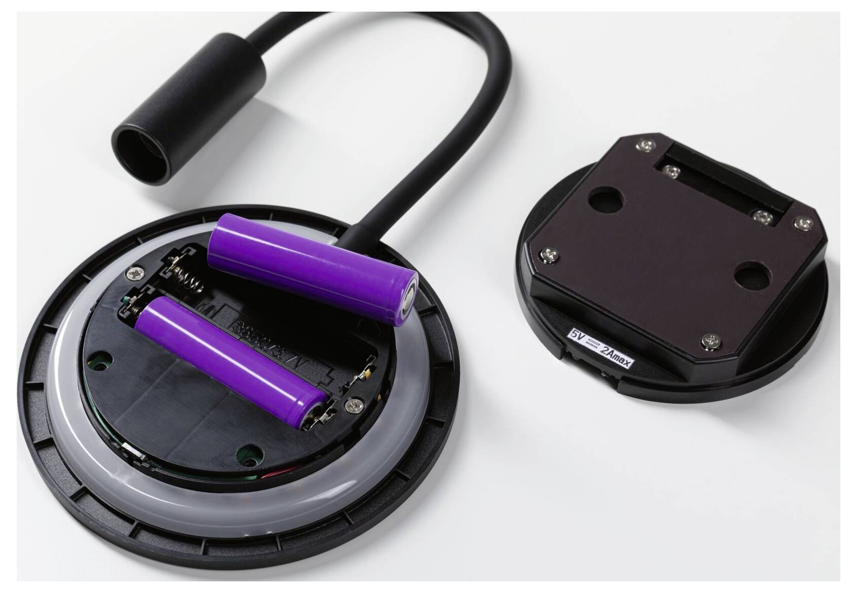 Öffnung des Batteriefachs mit zwei violetten wiederaufladbaren Batterien und einer abgelösten schwarzen Abdeckung auf weißem Hintergrund.