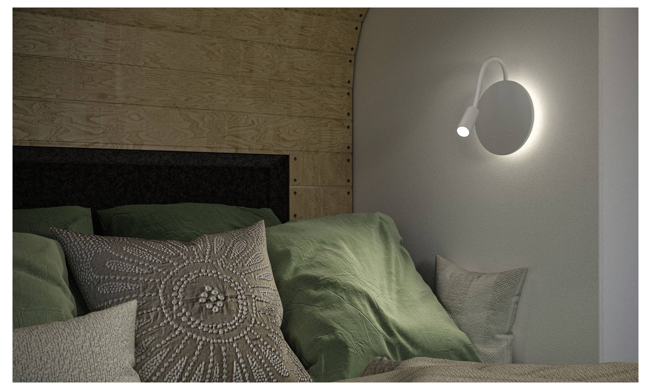 Gemütliche Schlafzimmerecke mit einem gepolsterten Bett, grüner Bettwäsche und gemusterten Kissen, beleuchtet von einer modernen Wandleselampe.