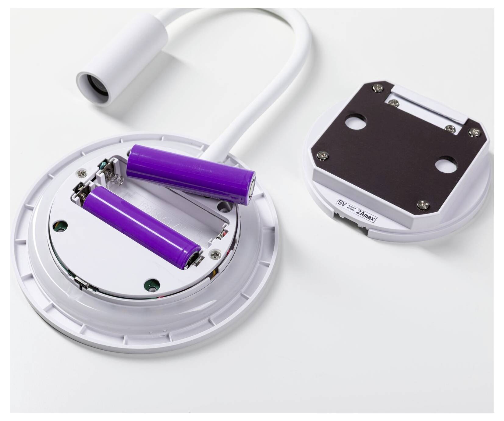 Offenes batteriebetriebenes Gerät mit zwei violetten zylindrischen Batterien, einem weißen Kabel und einem abgelösten Deckel auf weißem Hintergrund.