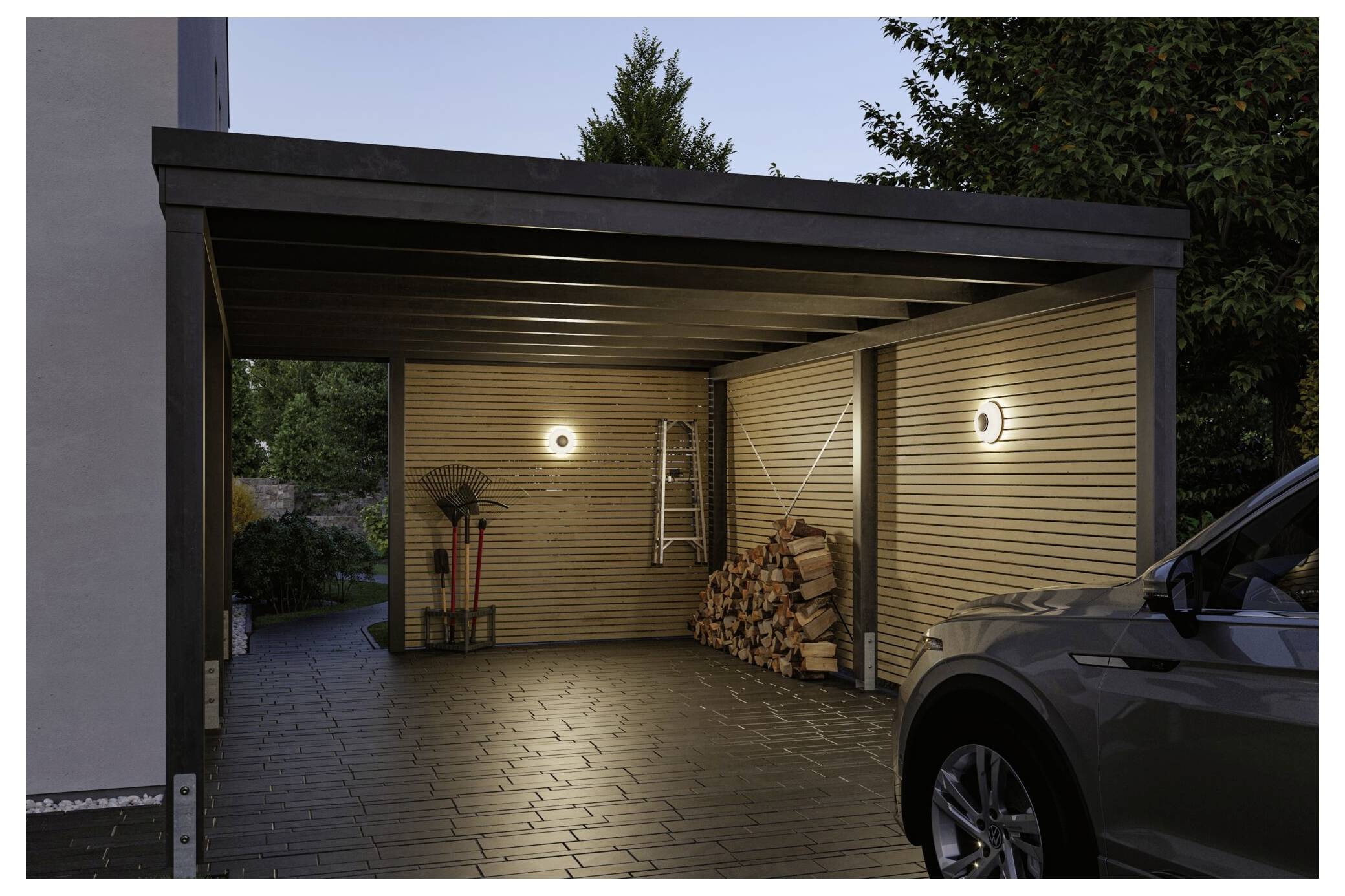 Überdachter Carport in der Dämmerung mit zwei Wandleuchten, gestapeltem Brennholz, Gartengeräten, einer Leiter und einem geparkten SUV auf der rechten Seite.